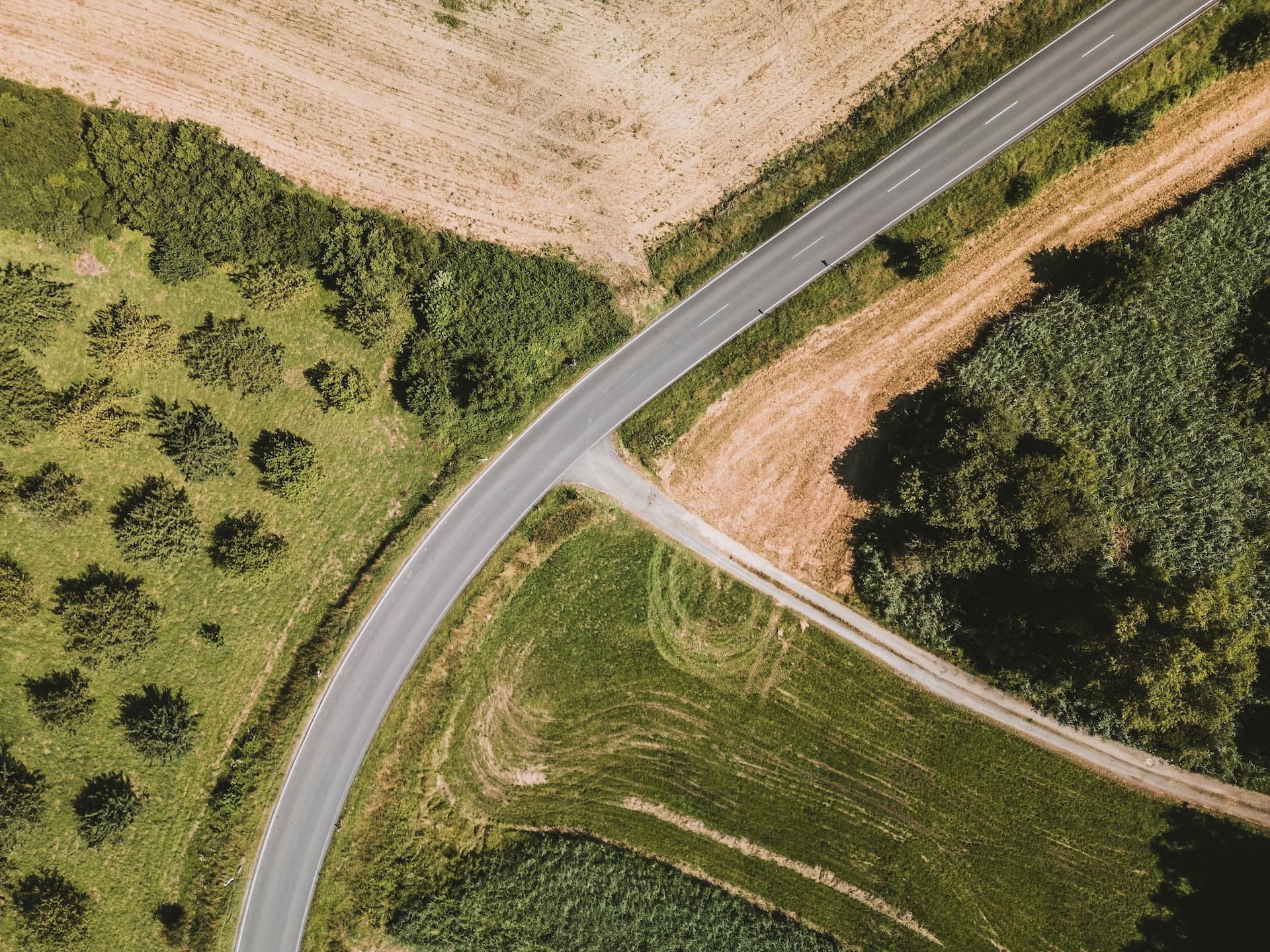 Aerial view of a two-lane road curving between green pasture, trees and a plowed field